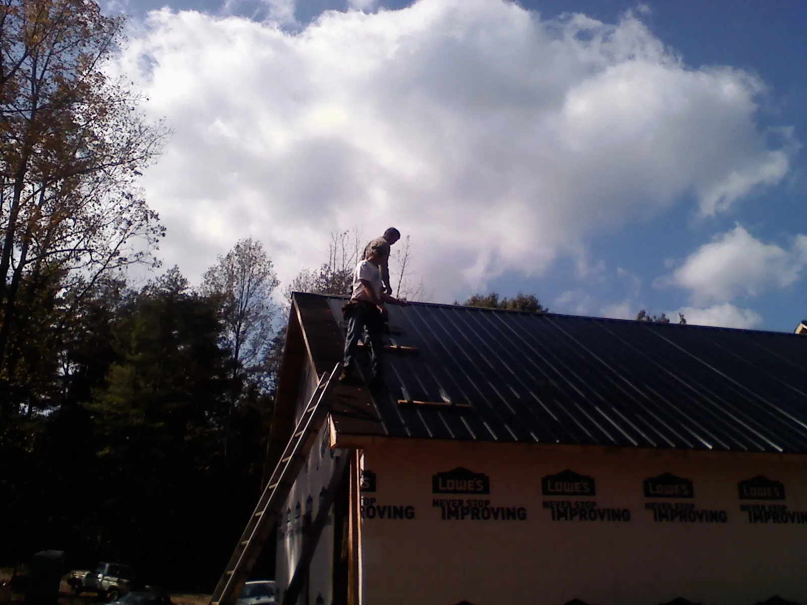 Roofer fastening dark metal panels high against a cloudy sky in Franktown