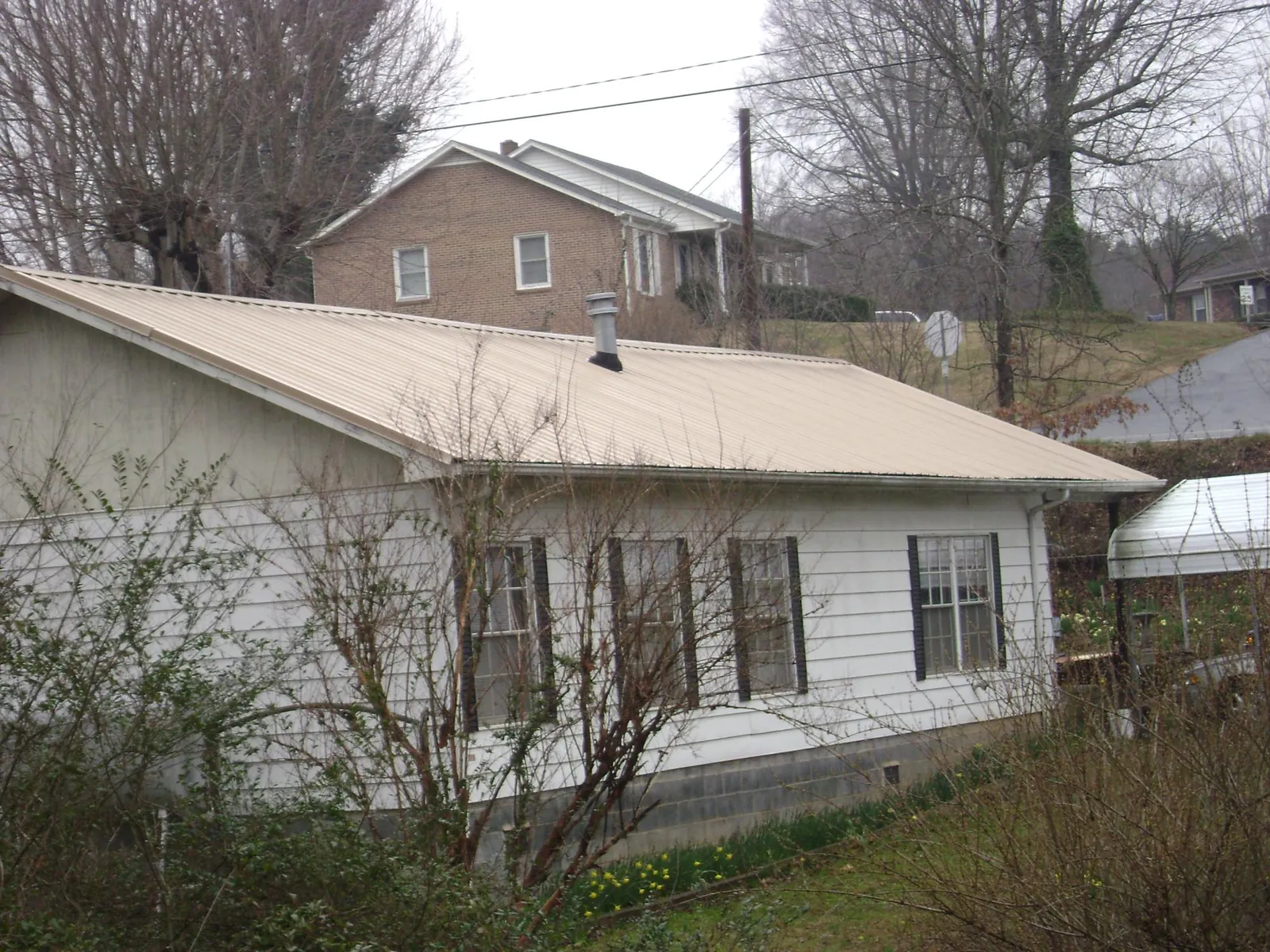 Tan metal roof on a white sided house set into a hillside — Commercial Roofing by Roofing Brothers in Franktown